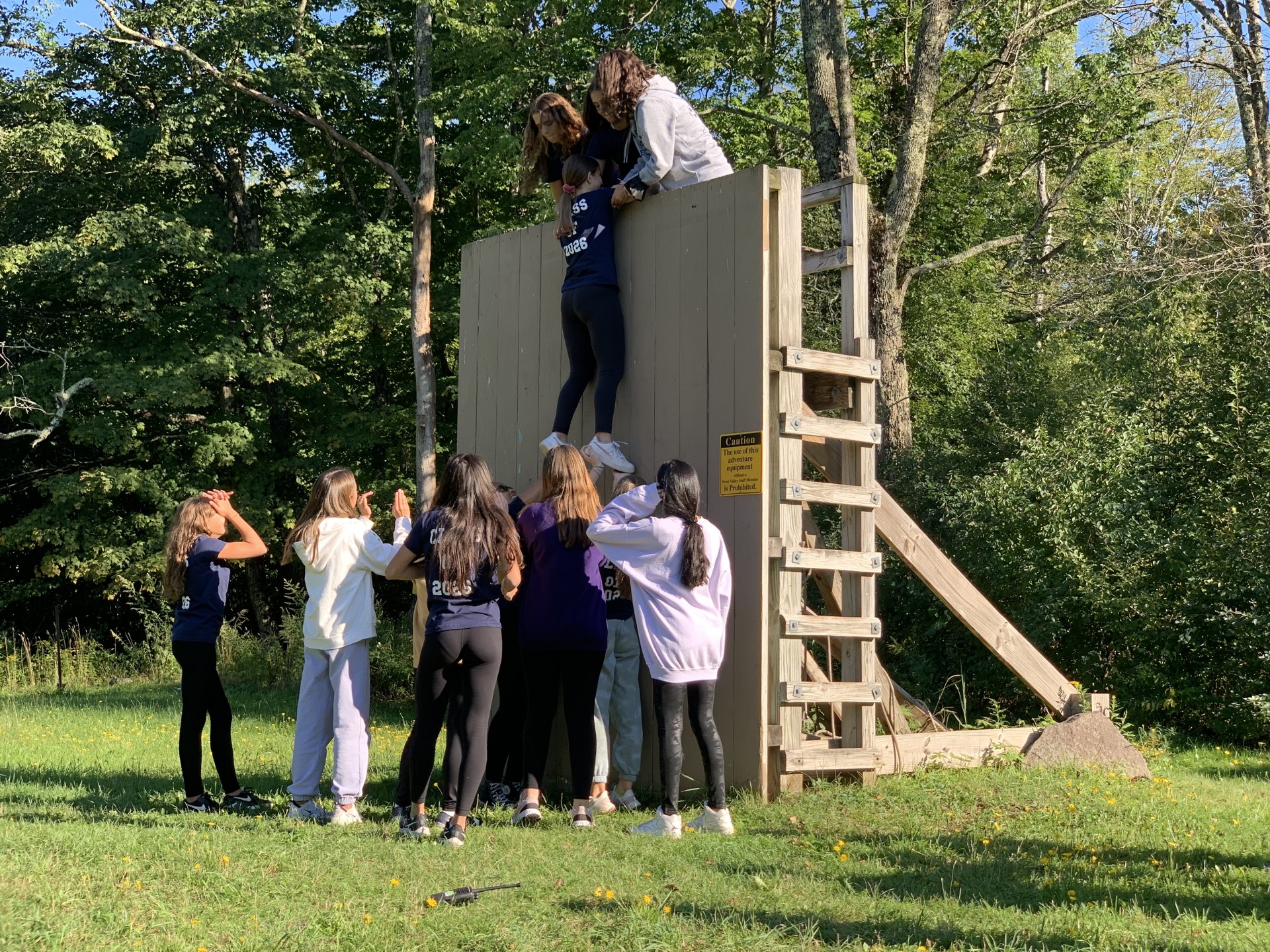 group of students helping a student over a wall