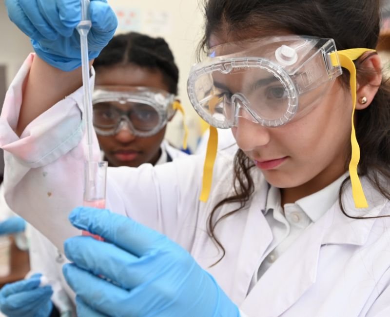 lower mid students using test tubes dressed in lab coats and safety goggles