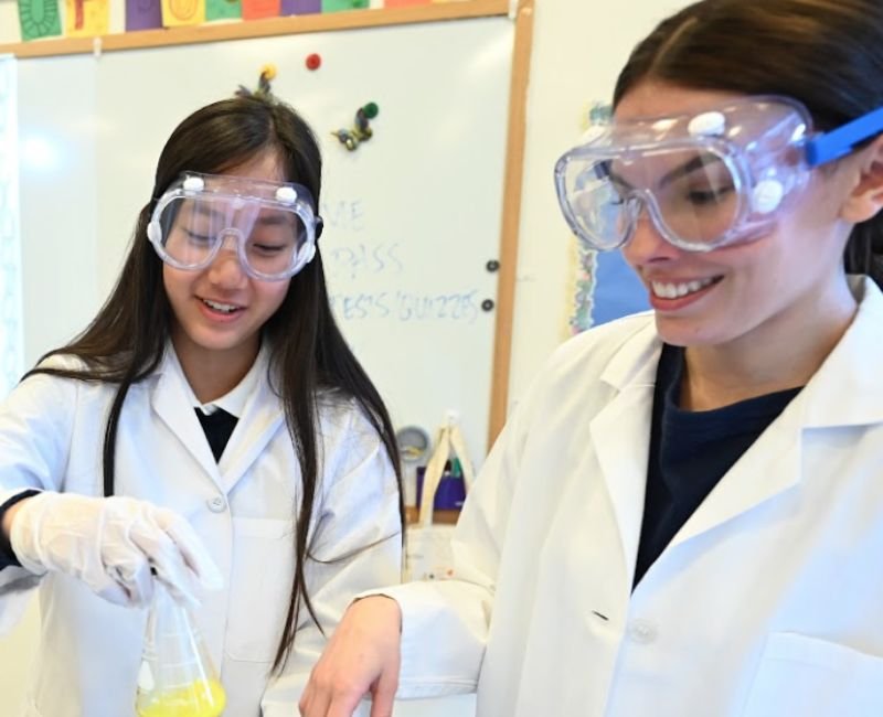 upper mid students using beakers dressed in lab coats and safety goggles